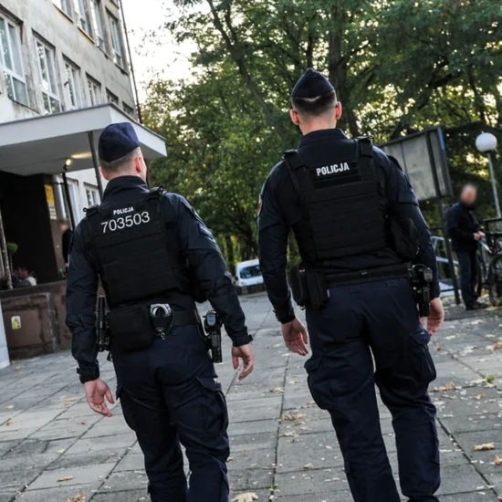 Policjanci idący przy budynku.