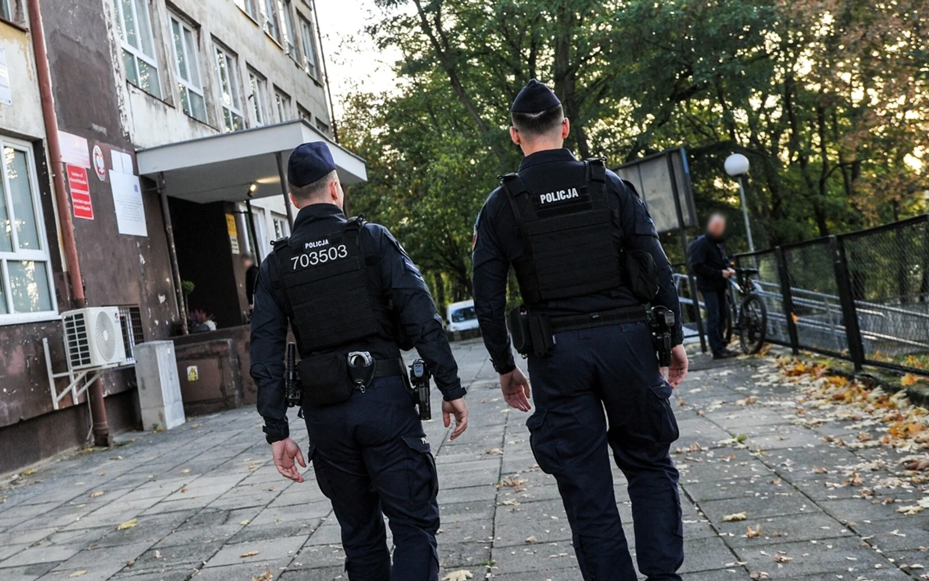 Policjanci idący przy budynku.