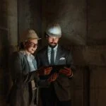 Dwie osoby w kaskach ochronnych przeglądają tablet we wnętrzu budynku.